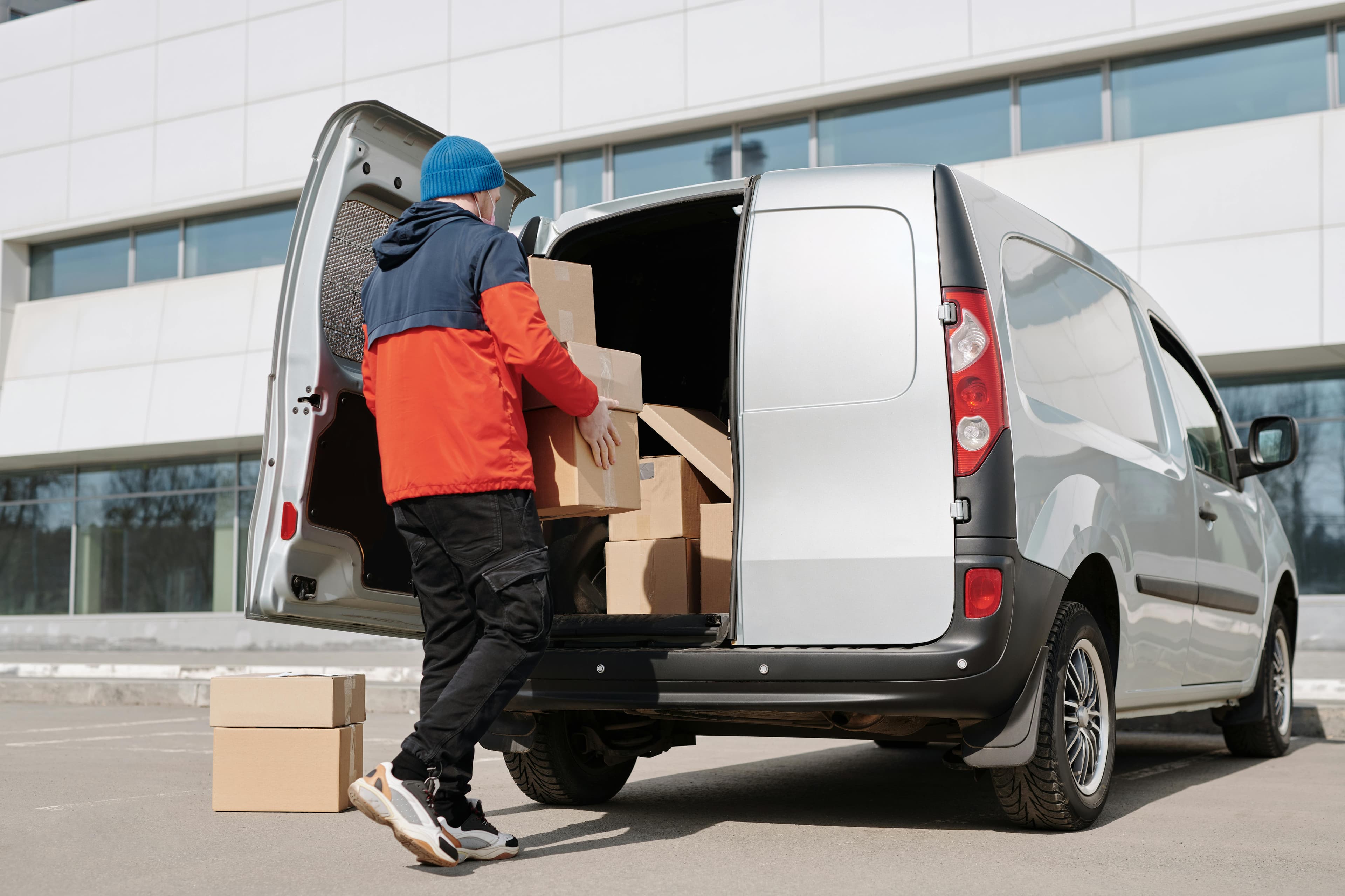 Delivery worker loading boxes into a white van at a commercial building
