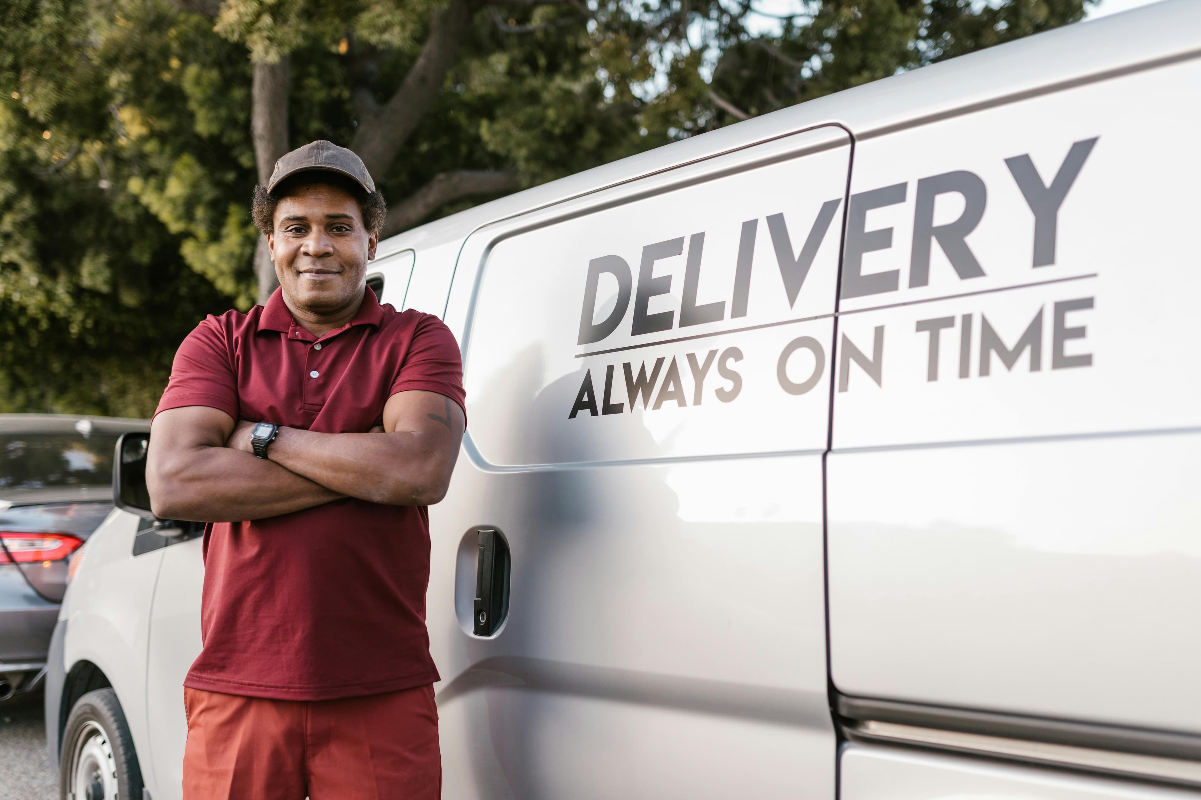 Professional delivery driver standing confidently in front of a white delivery van with 'DELIVERY ALWAYS ON TIME' branding