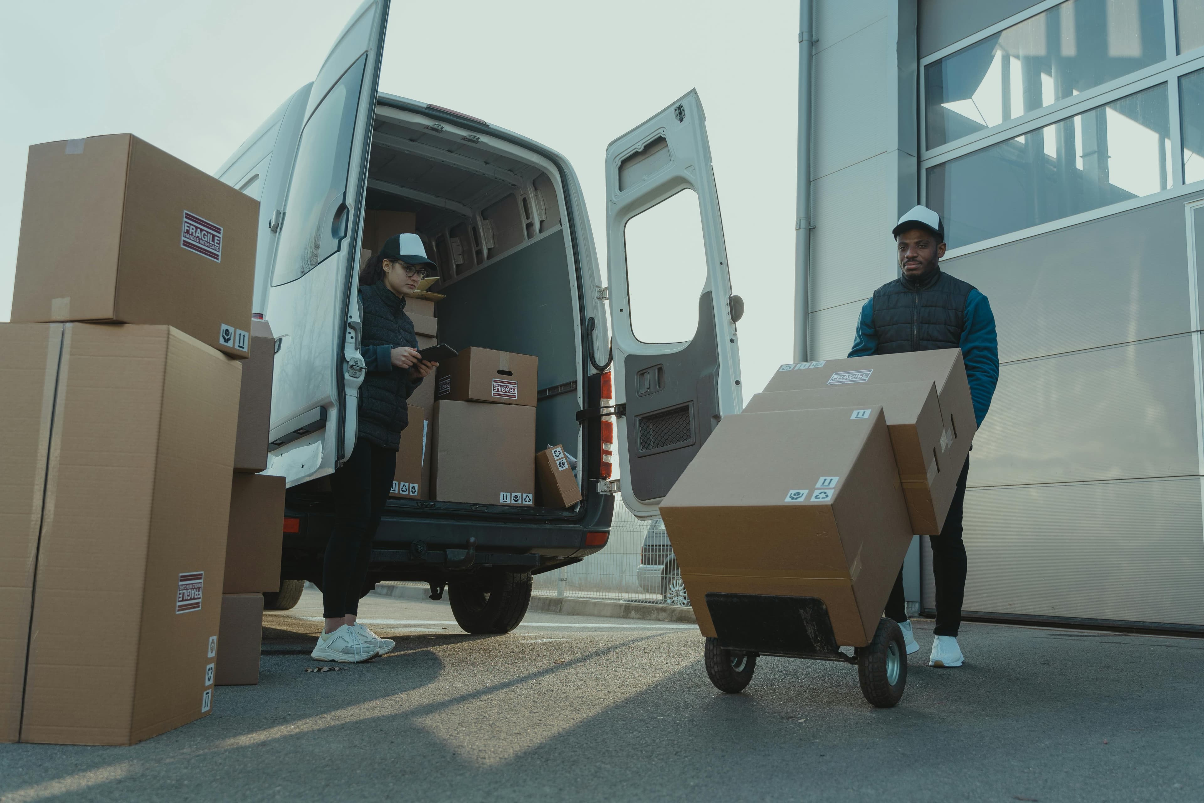 Delivery team loading large boxes onto a dolly from an open van